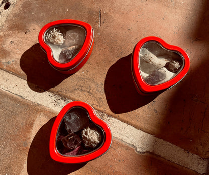 May include: Three red heart-shaped tin boxes filled with various crystals and stones. Each box features a clear window showcasing the contents. The crystals include clear quartz, amethyst, and selenite.  These decorative boxes are perfect for storing small trinkets or crystals.